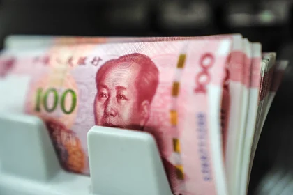 Close-up of a stack of Chinese 100-yuan banknotes held in a money holder or wallet, pink and red in color with a portrait visible in the foreground (RMB).