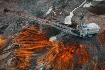 Massive mining crane looms over a terraced open-pit with orange-brown earth and dark rock walls