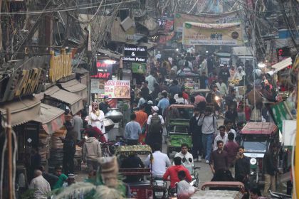 A crowded street market filled with pedestrians, rickshaws, and stalls under tangled overhead wires.