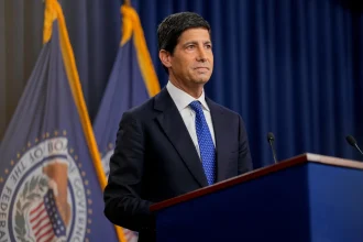 A Federal Reserve official speaking at a podium in front of flags